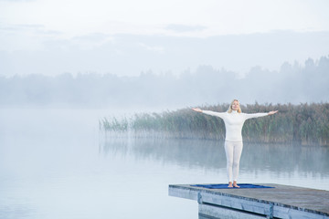 Fototapeta na wymiar Young woman feels the freedom in the mist on the lake footbridge in the morning. Peaceful atmosphere. Foggy air.