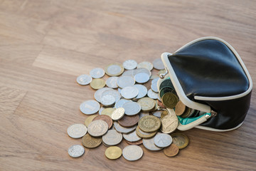 Black leather wallet with different coins on the wooden surface