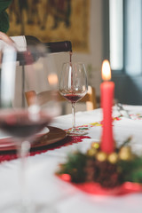 Close up on a hand pouring a glass with red wine on a table set for christmas - happy hour, beverage, relax concept