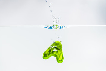 Green wooden alphabet A drop in the water with white background and selective focus