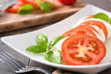 Caprese salad with mozzarella cheese, tomatoes and basil on rustic wooden table

