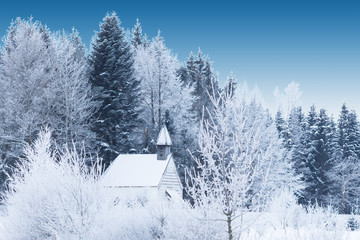 Snow-capped little wooden chapel in frosty winter forest