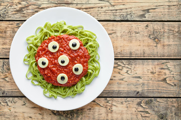Spooky halloween monster green spaghetti pasta holiday decoration party food with fake blood tomato sauce and many mozzarella eyeballs on vintage wooden table background
