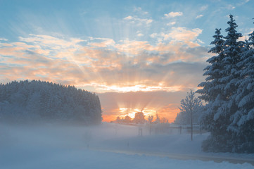 Winter morning snowy scenery with dawn sunlight rays breaking cl