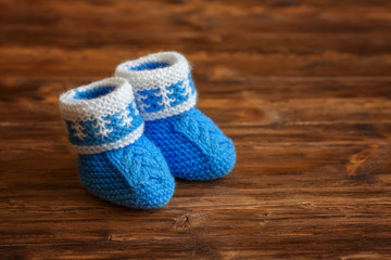 Fototapeta na wymiar Blue hand made crochet baby booties on wooden background, copyspace