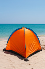 Una tenda arancione su una spiaggia bianca con acqua cristallina