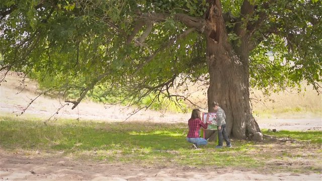 Mother and son paint the colorful pictures under a tree near the forest