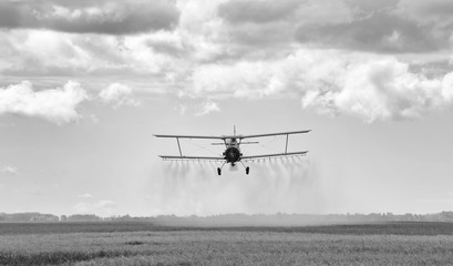 Obraz premium Spray plane swooping down and spraying chemical on a agriculture field at harvest in black and white