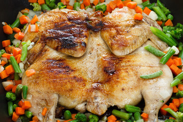 Whole grilled chicken with vegetables in a frying pan