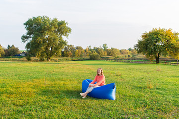 Naklejka na ściany i meble Young woman sitting on a air sofa against the background of green meadow
