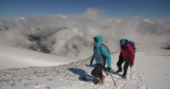 Close Up on Two Mountaineers Cross Snow Field Above Clouds.