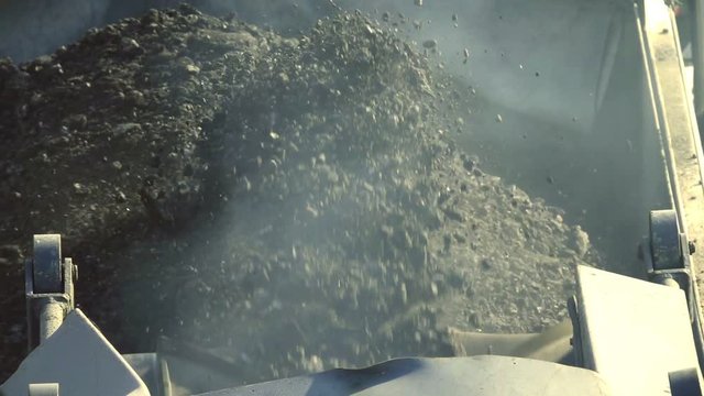 Cold milling machine, milled asphalt falls into the back of the truck, close up, top view, slow motion