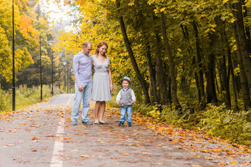 Fototapeta premium Happy young family walking down the road outside in autumn nature.