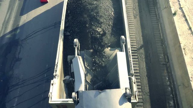 Cold milling machine, milled asphalt falls into the back of the truck, top view, slow motion