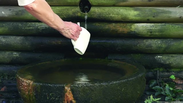 woman pours a cup of water from the source 