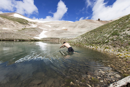 Man diving into lake by mountains against sky