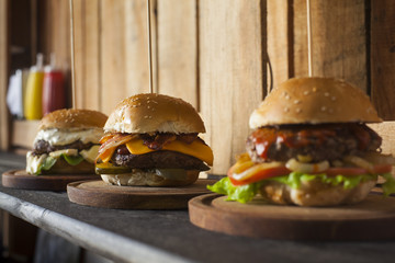 Three tasty different hamburgers on a wooden table.