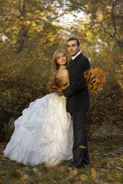Beautiful wedding couple kissing,embracing in autumn park under sunbeam,newlyweds holds autumnal leaves bouquet. Young couple in love/Wedding couple at autumn park.Married couple in the wedding day