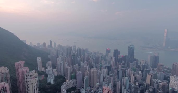 Beautiful aerial shot of many high  skyscrapers covered with sunset fog or haze in Hong Kong, China. Top view of Victoria Harbour from Victoria Peak at sunset. City skyline.
