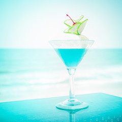 Blue margarita cocktail with lime fruit and cherry decoration at tropical ocean beach. Vintage style, hipster colors image with copy space for party invitation text