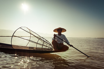 Burmese fisherman on bamboo boat catching fish in traditional way with handmade net. Inle lake, Myanmar (Burma) travel  destination