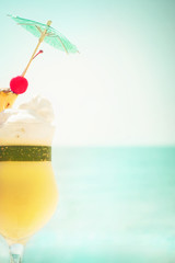 Pina colada cocktail with fruits and umbrella decoration at tropical ocean beach. Vintage style, hipster colors image with copy space for party invitation text