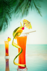 Tequila sunrise and long island cocktails with fruits and umbrella decoration at tropical ocean beach with palm trees. Vintage style, hipster colors image with copy space for party invitation text