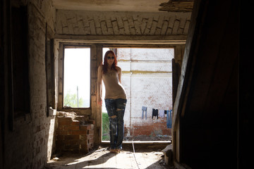 Obraz na płótnie Canvas Young fashionable attractive sexy girl in glasses and jeans stands inside a destroyed building at sunny summer midday