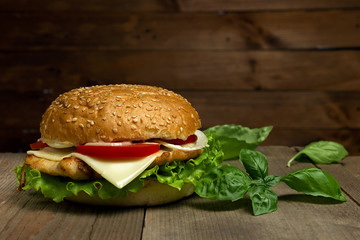 Home made hamburger with cheese, tomatoes and basil  on wooden background. Fastfood meal.