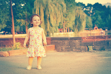 Naklejka premium A baby on the background of nature. Child near the lake. Kid walking on the street in the summer. Summer scene with little girl. Summertime, springtime Concept of childhood