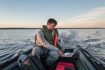 Man is seating in the boat and working with laptop