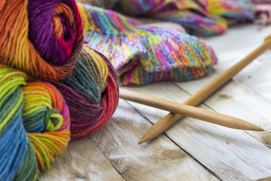 Colorful skeins of wool with knitting needles and sweater on wooden background