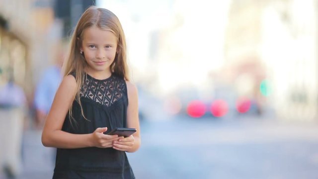 Adorable little girl with smart phone at warm day outdoors in european city