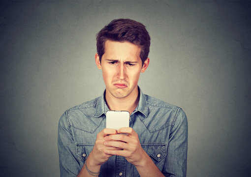 Upset stressed man holding cellphone disgusted with message received
