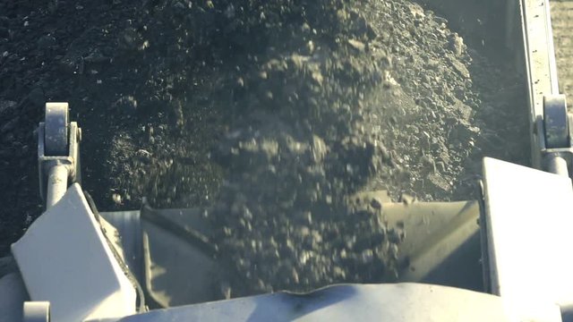 Cold milling machine, milled asphalt falls into the back of the truck, close up, top view, slow motion