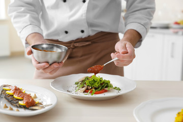 Young chef cook putting tomato sauce on dishes