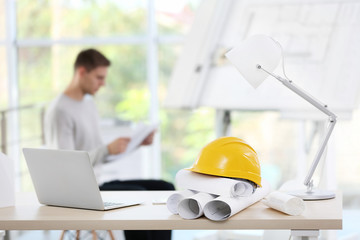 Helmet with laptop and blueprints on table and engineer on blurred background