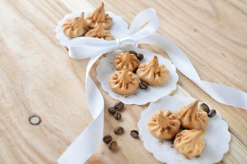 Vanilla meringue cookies on wooden background with copy space. Cakes with white ribbon and coffee.