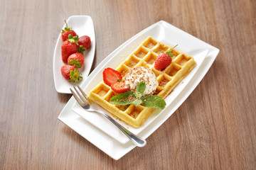 breakfast dessert - golden waffles with ice cream and fresh sliced strawberries sprinkled with sugar and chocolate