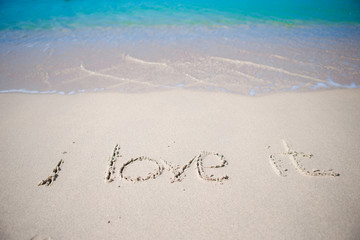 Word i love it handwritten on sandy beach with soft ocean wave on background