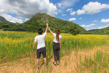 Asian couple holding hands up relaxing in nature with sunhemp flower field in thailand