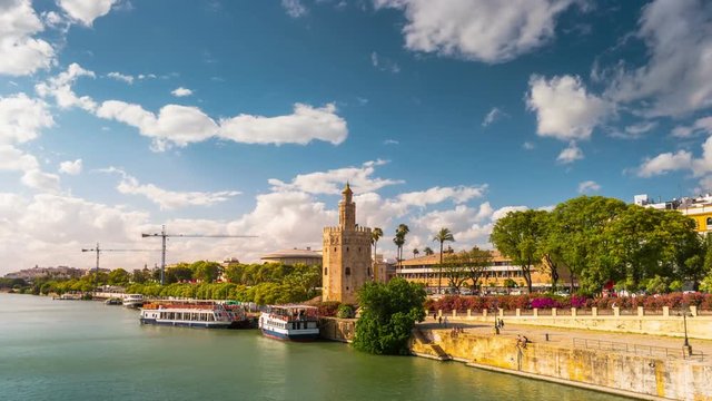 View of Golden Tower, Torre del Oro, of Seville, Andalusia, Spain over river Guadalquivir at sunset. Timelapse with clouds flying over historic buildings.