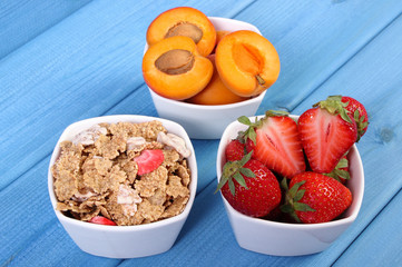 Fresh fruits, wheat and rye flakes in bowl on blue boards, healthy lifestyle