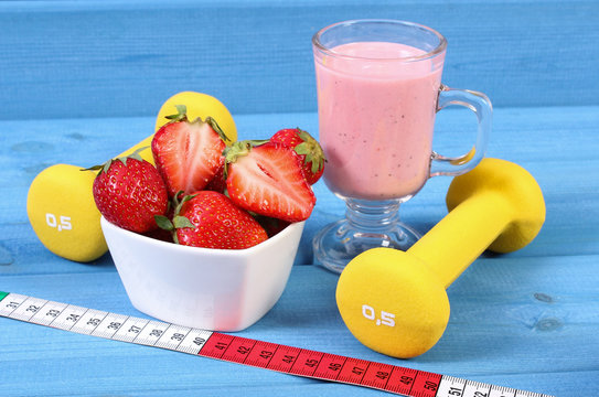 Fresh strawberries, milkshake, dumbbells and centimeter on boards, healthy and sporty lifestyle