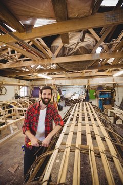 Portrait of man standing near a wooden boat frame