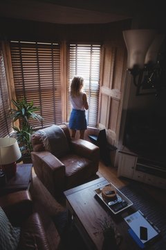 Rear view of woman looking through window in living room