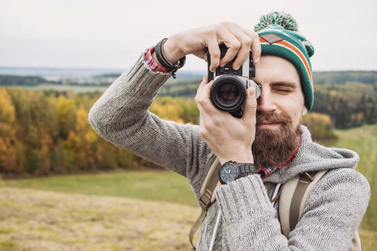 Young cheerful man photographer takes images with camera outdoors. Travel and active lifestyle concept