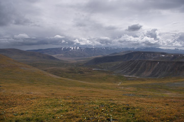 A wide valley on the Ukok plateau, under a cloudy sky on the background of mountain ranges, the Altai mountains, Siberia, Russia