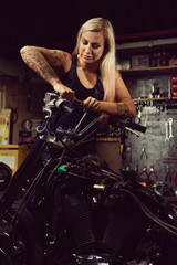 Naklejka na ściany i meble Blond woman mechanic repairing a motorcycle in a workshop
