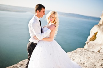 Fototapeta na wymiar Charming bride and elegant groom on landscapes of mountains, water and blue sky at sunny weather